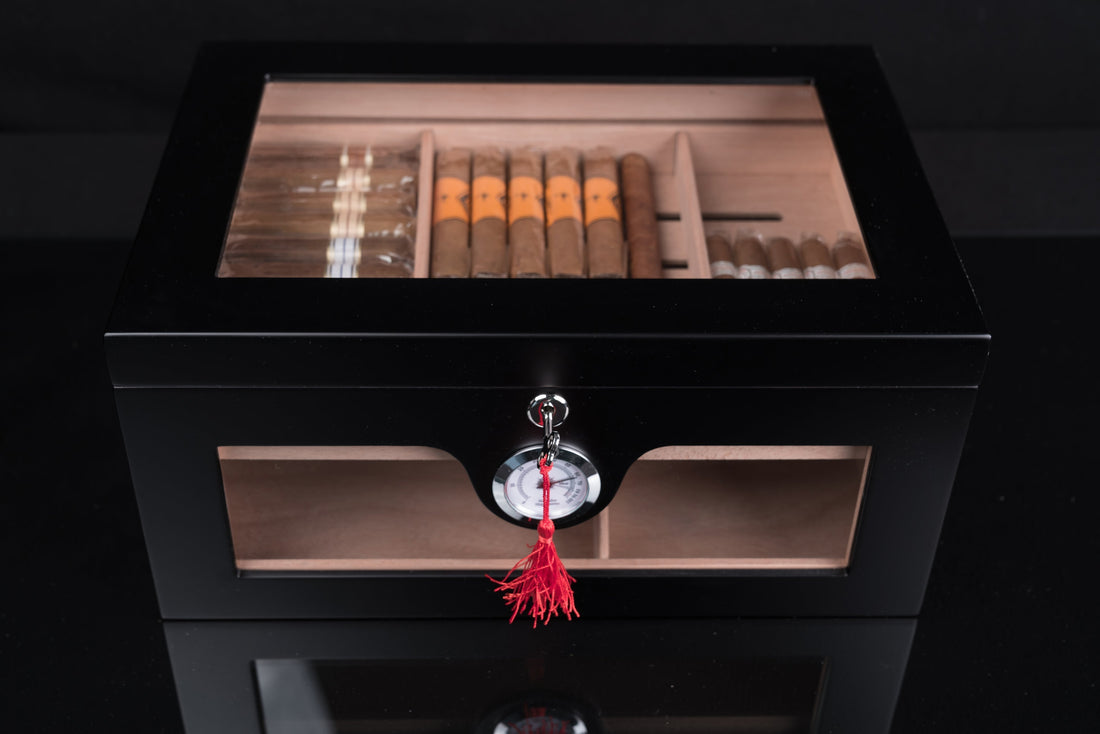 The best desktop humidor on the market with a satin black wooden exterior, a glass top, and a mounted external hygrometer.