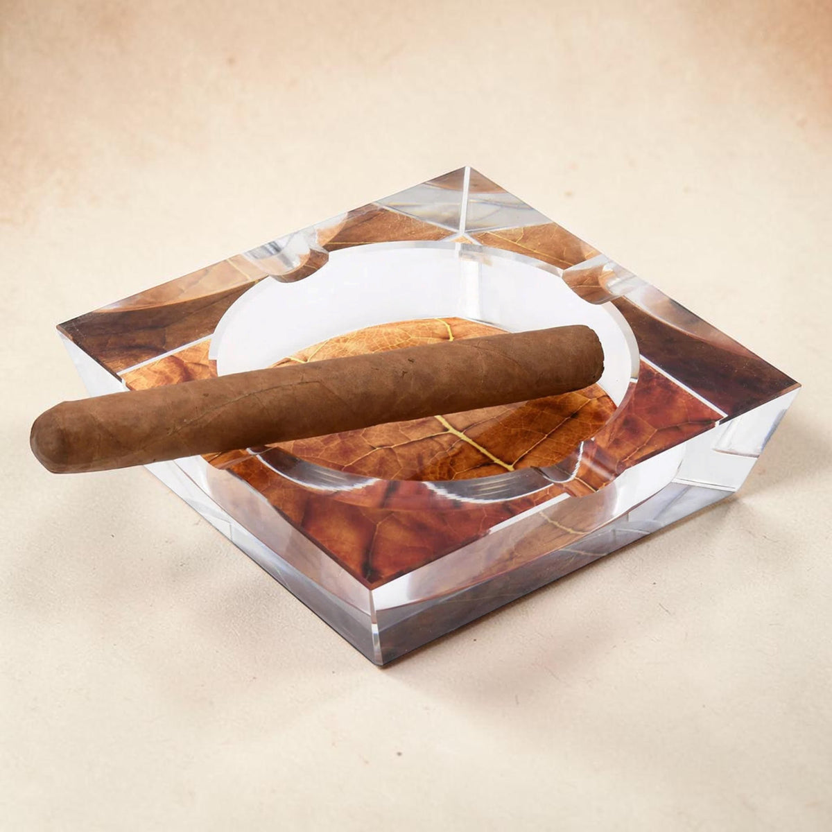 A square K9 crystal cigar ashtray with four cigar rests and a decorative tobacco leaf design visible through the crystal. 