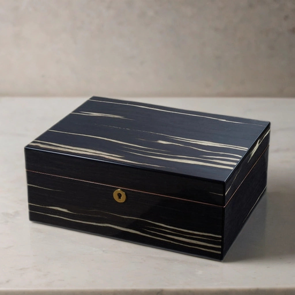 Dark wooden desktop cigar humidor with gold accents on a marble surface